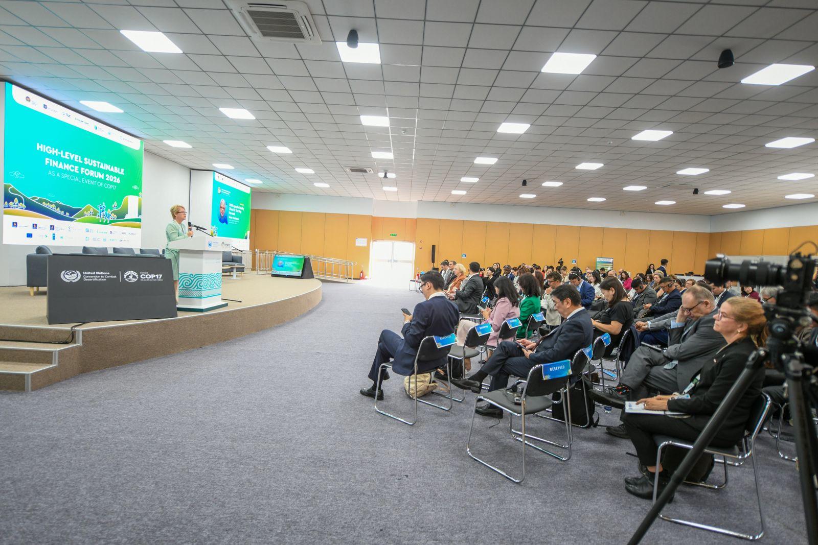 Audience seated in a modern conference room watching a presentation on stage with a large screen.
