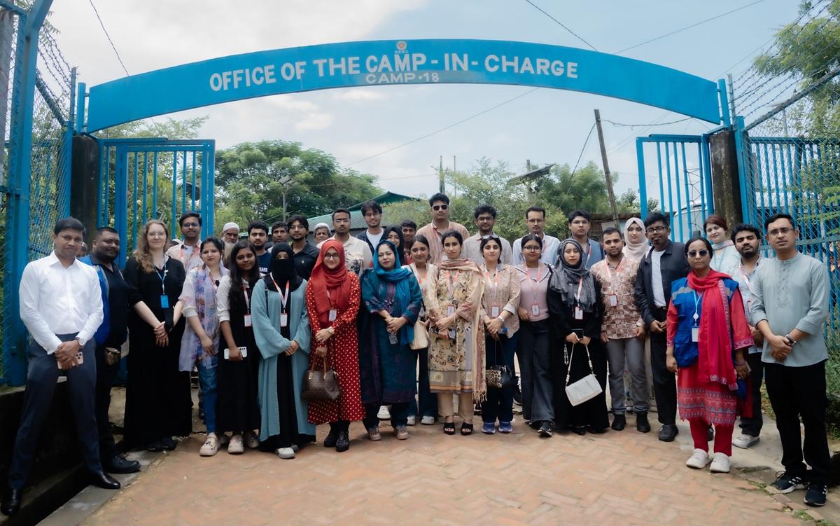 Group of men and women posing under a blue arch that reads Office of the Camp-In-Charge.