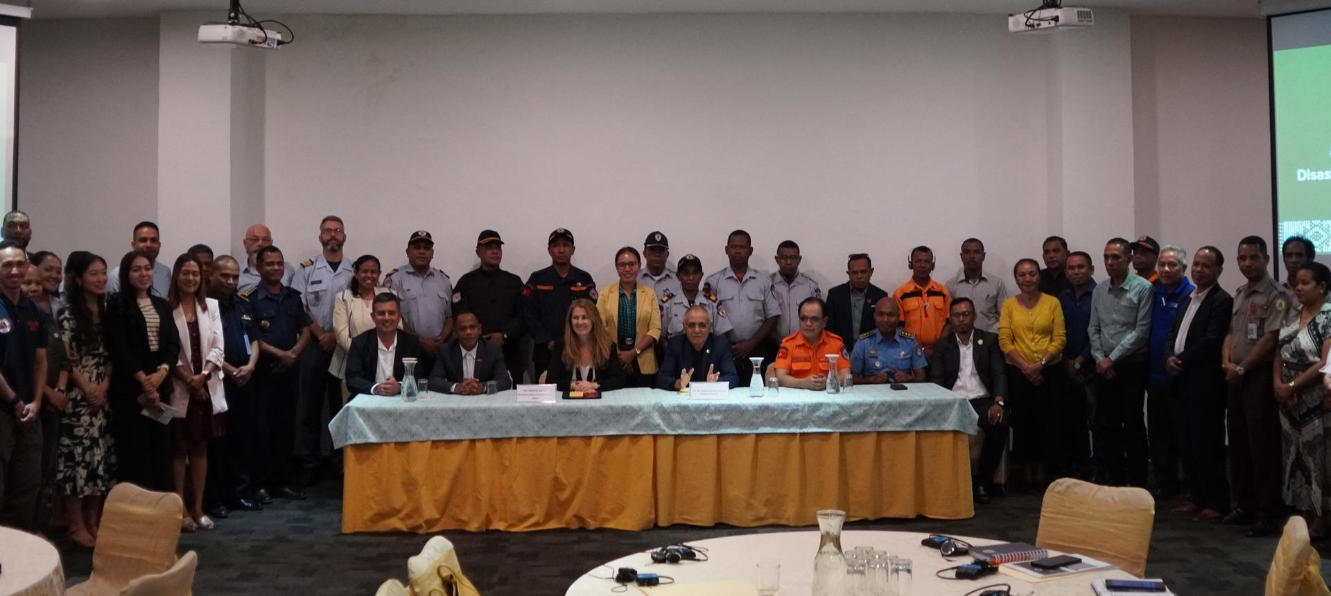Group photo of conference attendees standing behind a long table in a meeting room.