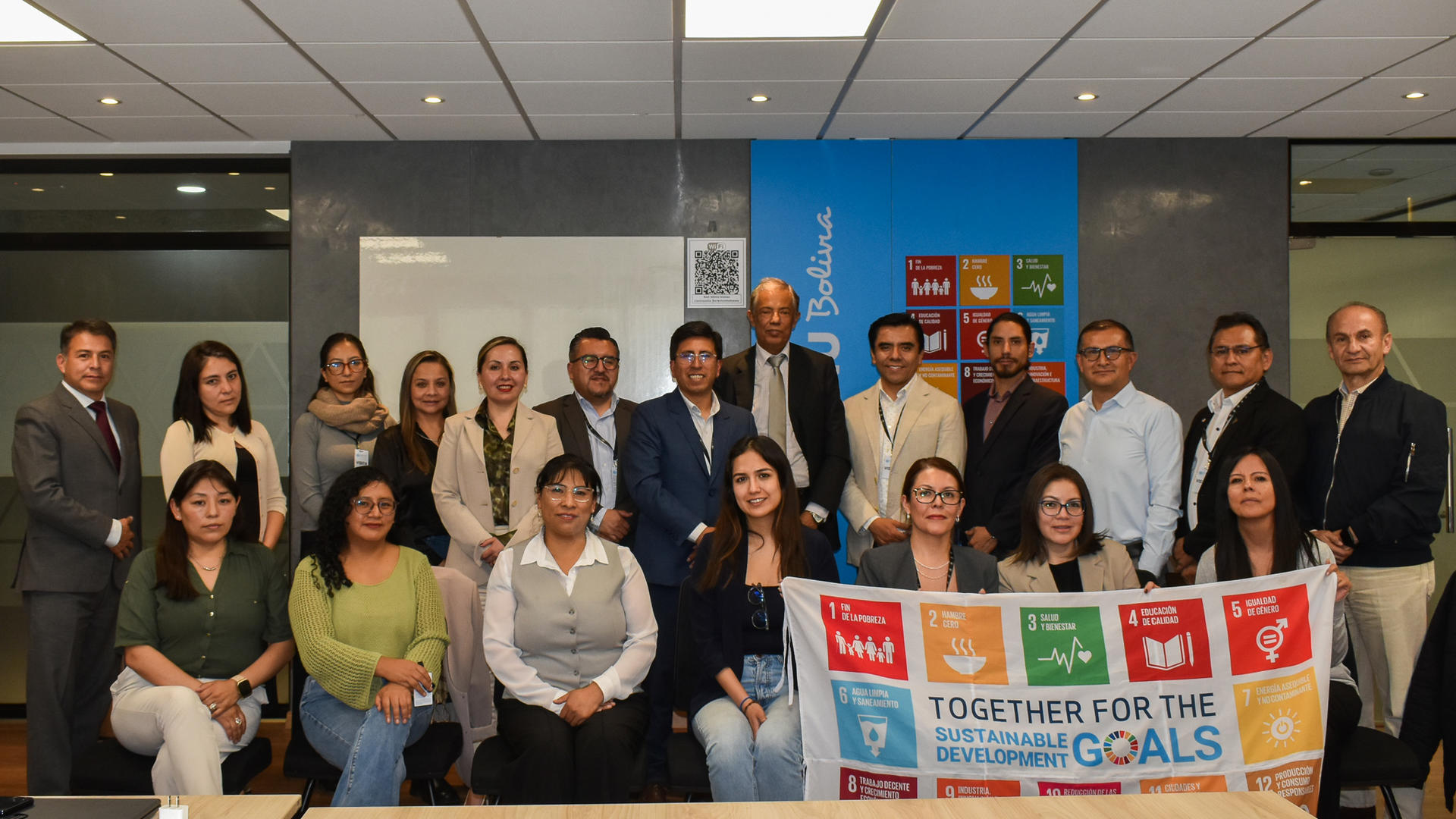 Group of diverse professionals posing in a conference room with a banner and SDG posters.