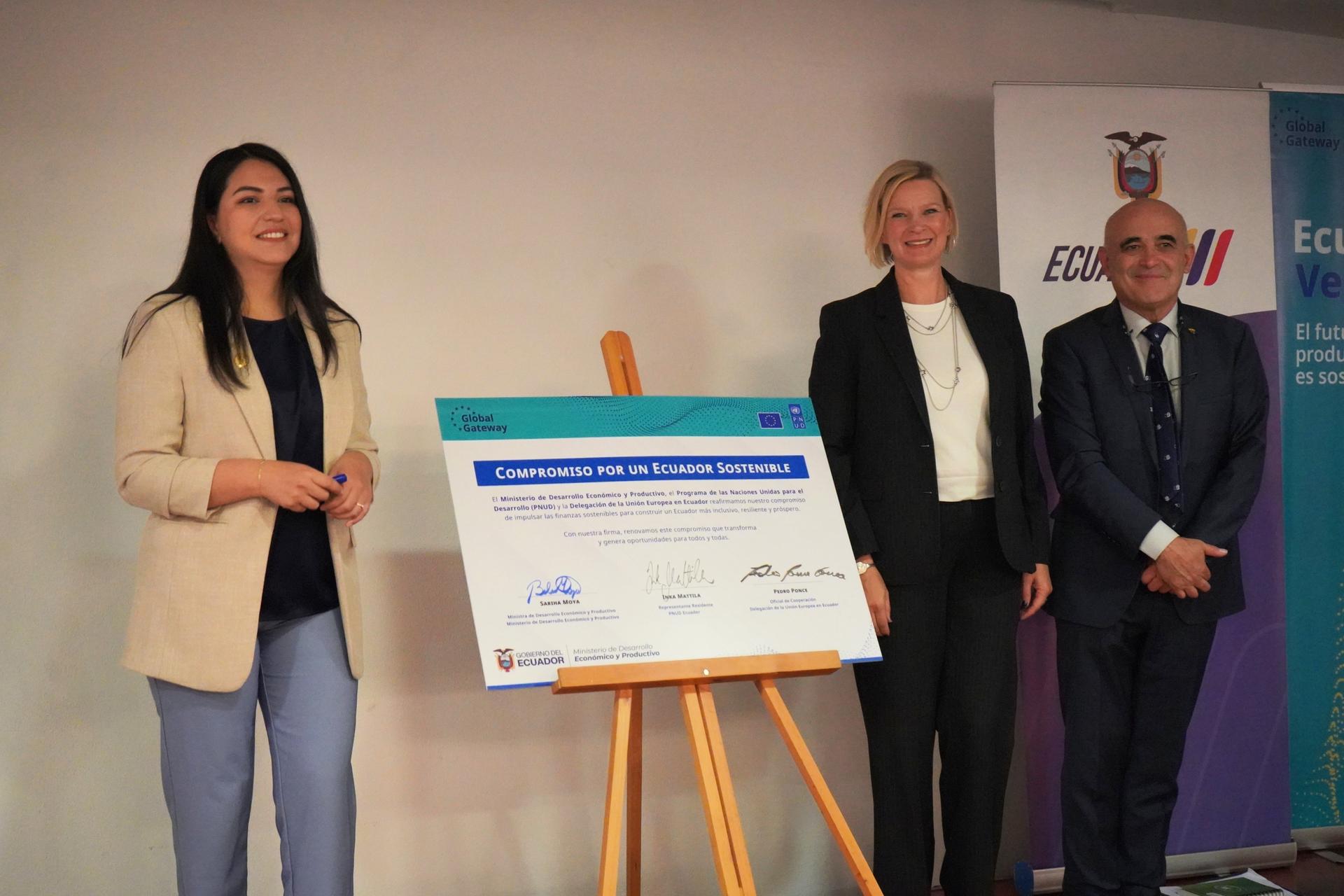 Four people in business attire stand on stage beside an easel displaying a large framed certificate.