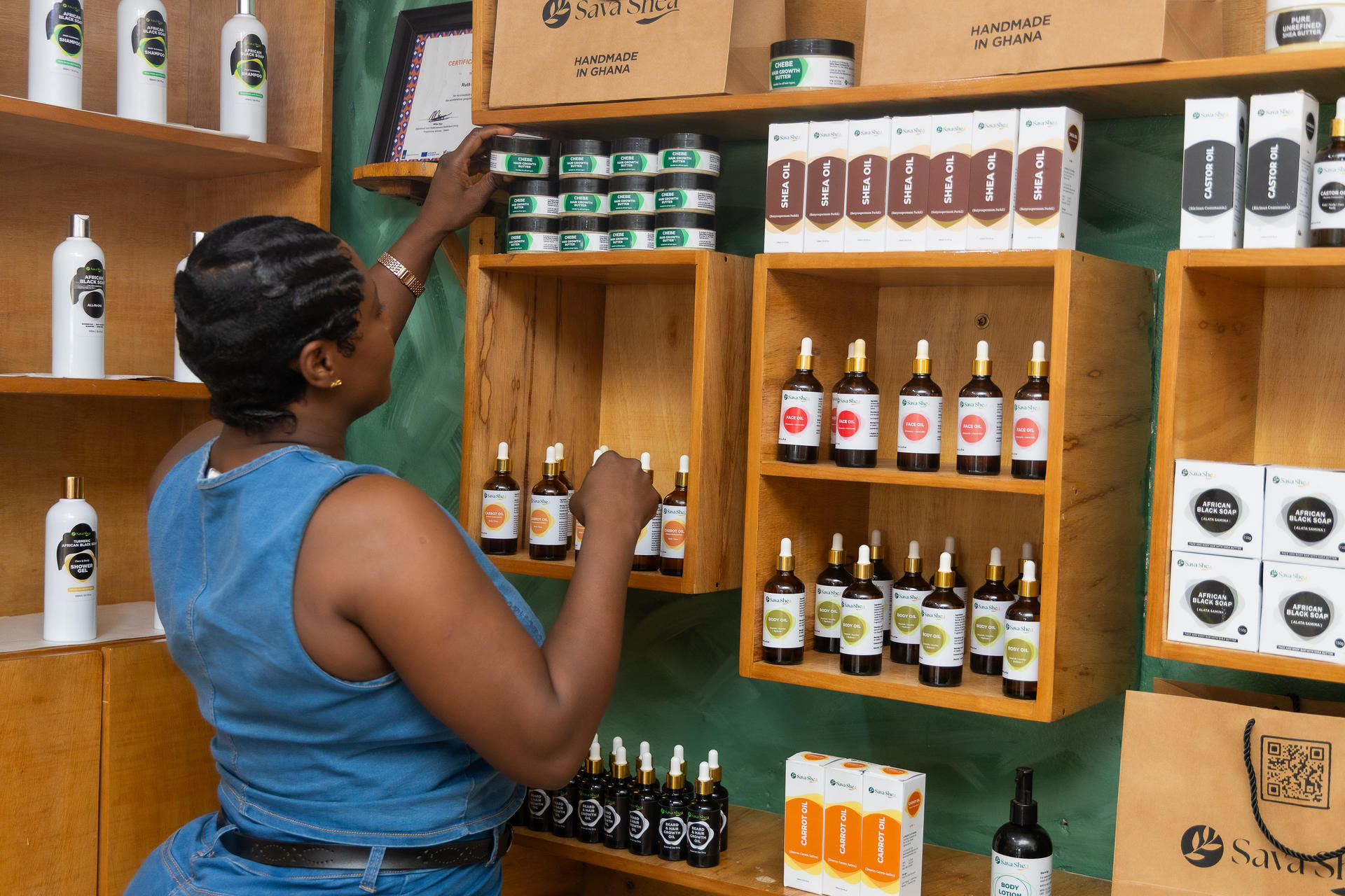 Person in a blue sleeveless top reaching for bottles on wooden shelves in a shop.