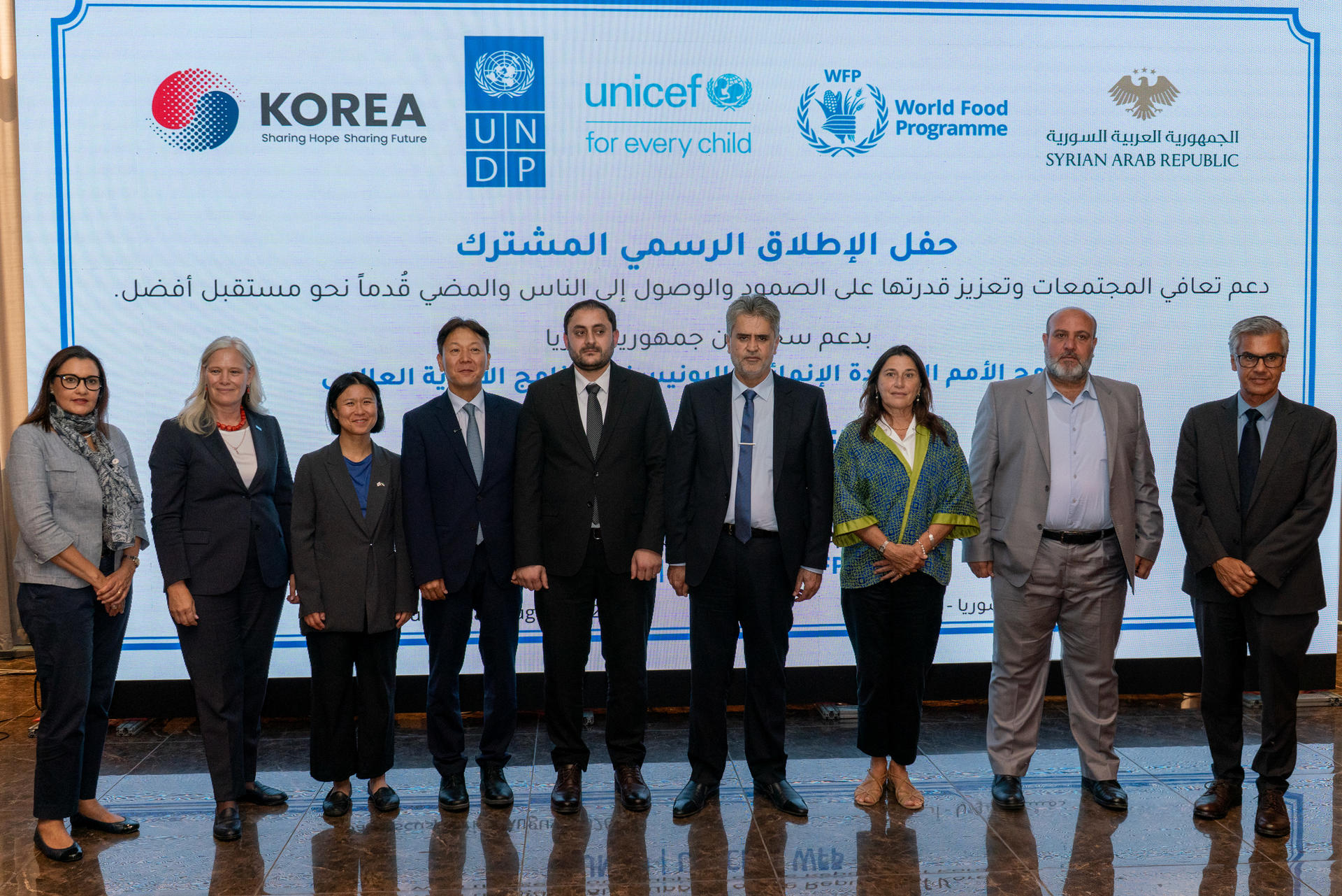 Group of professionals standing on stage in front of a banner displaying Korea and UNICEF logos.