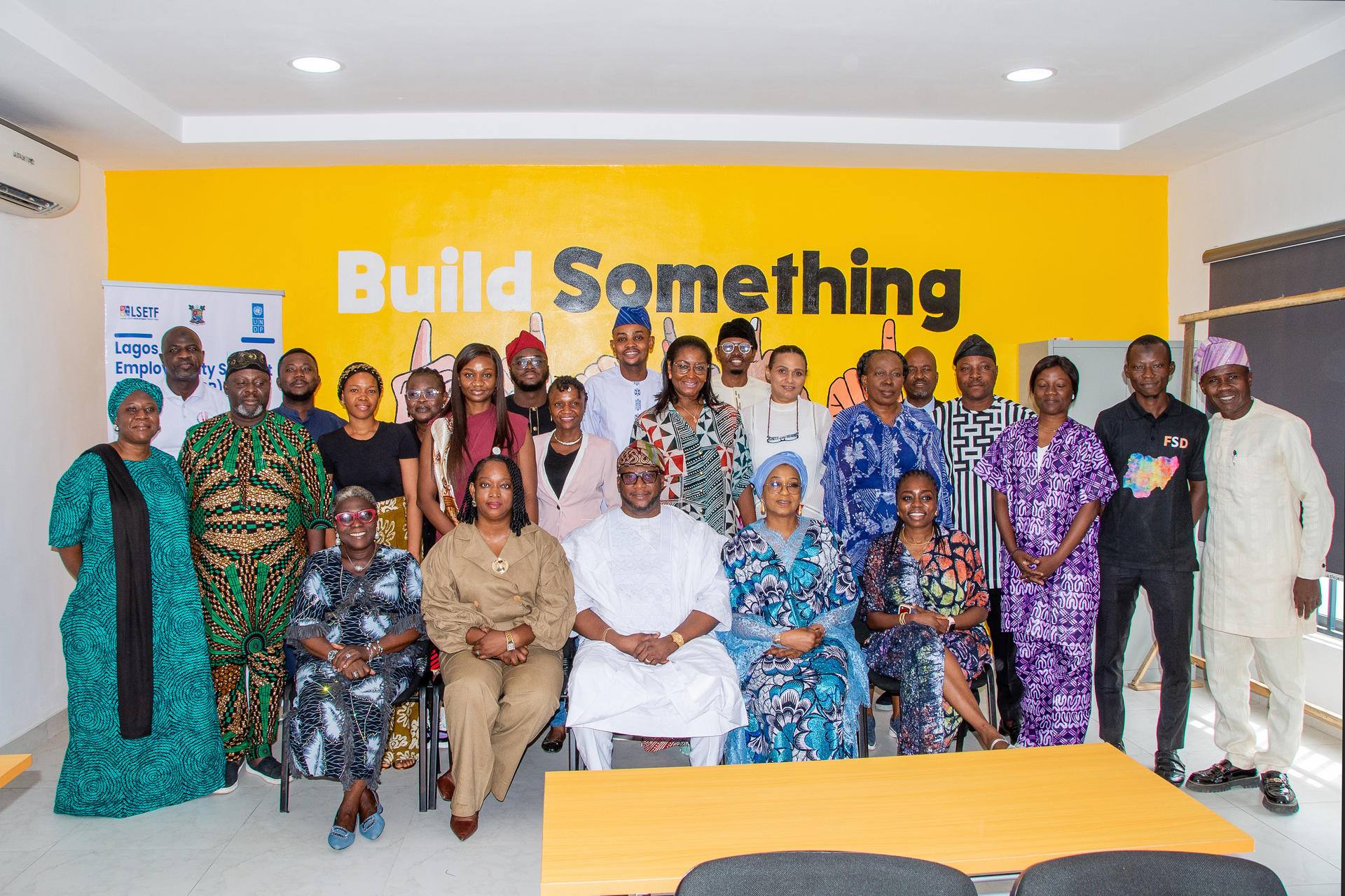 Group of diverse people posing in a room with a yellow banner that reads Build Something.