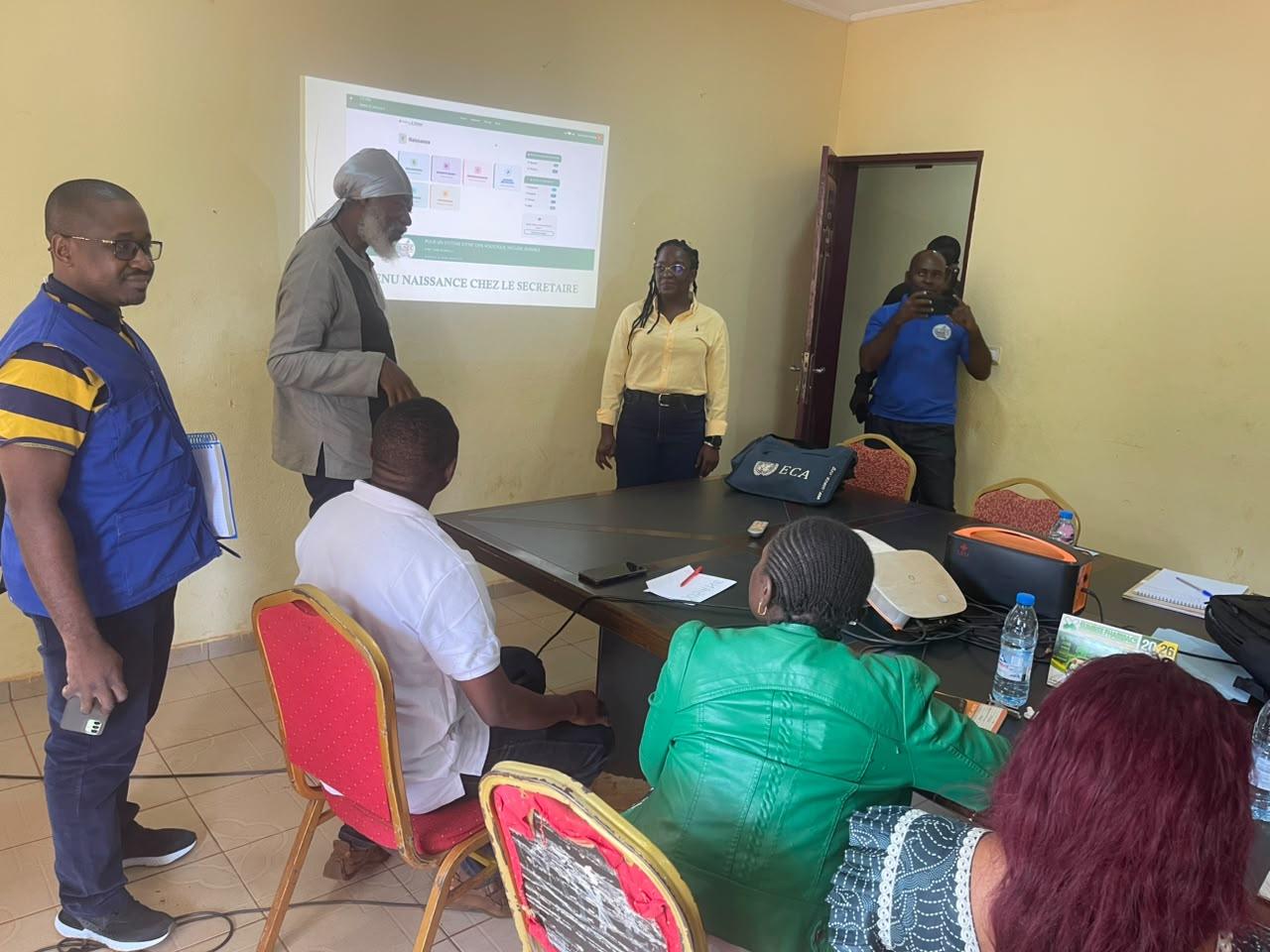 Small classroom meeting with a presenter near a projector screen and seated attendees.