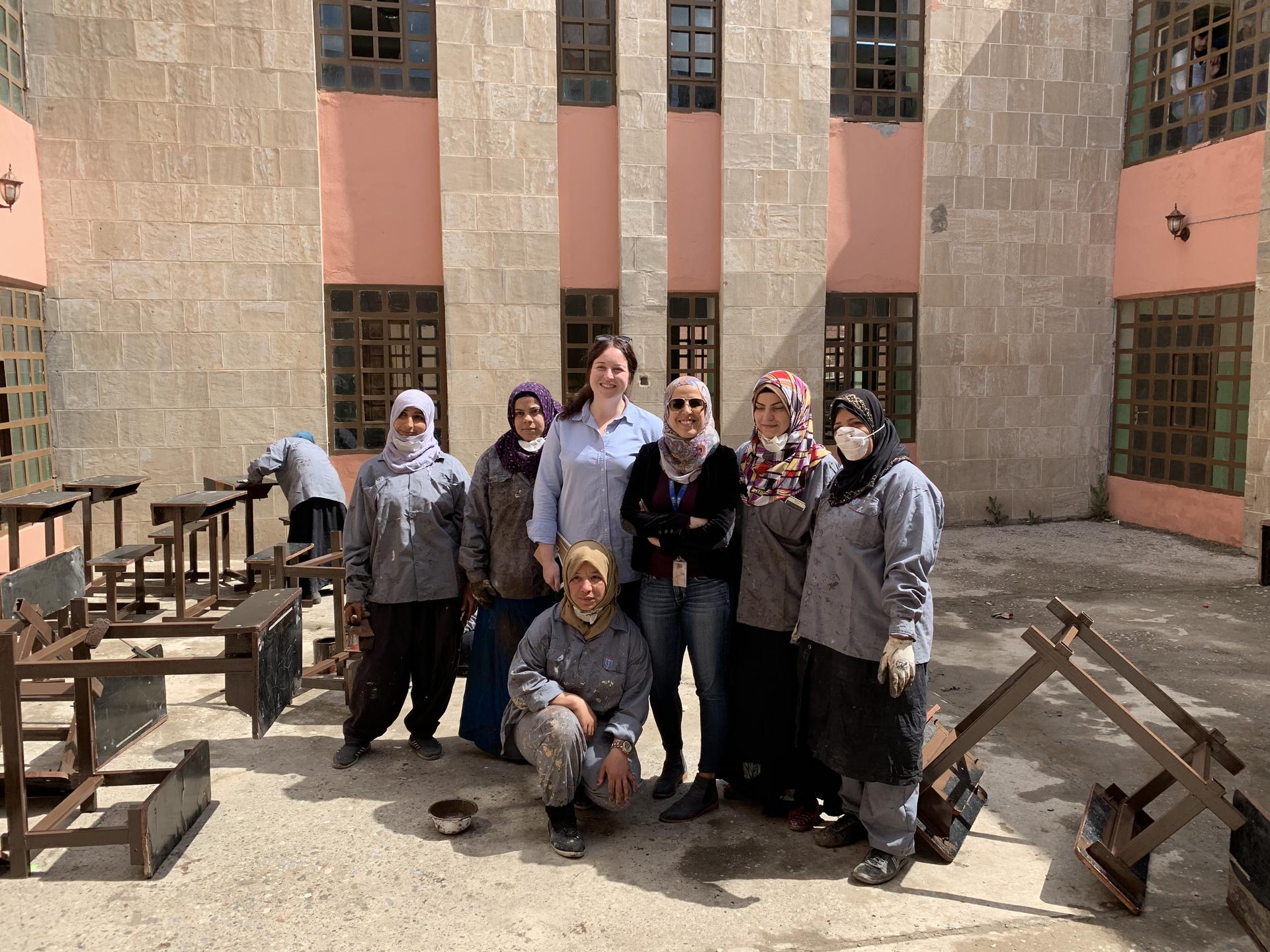 Group of people posing in a sunny courtyard with pink stone walls and wooden benches.