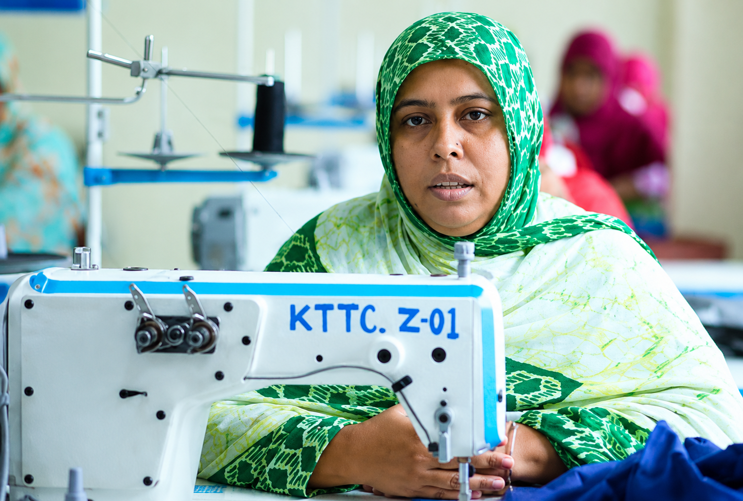 Photograph of a woman in a green hijab sewing at a machine in a textile workshop.