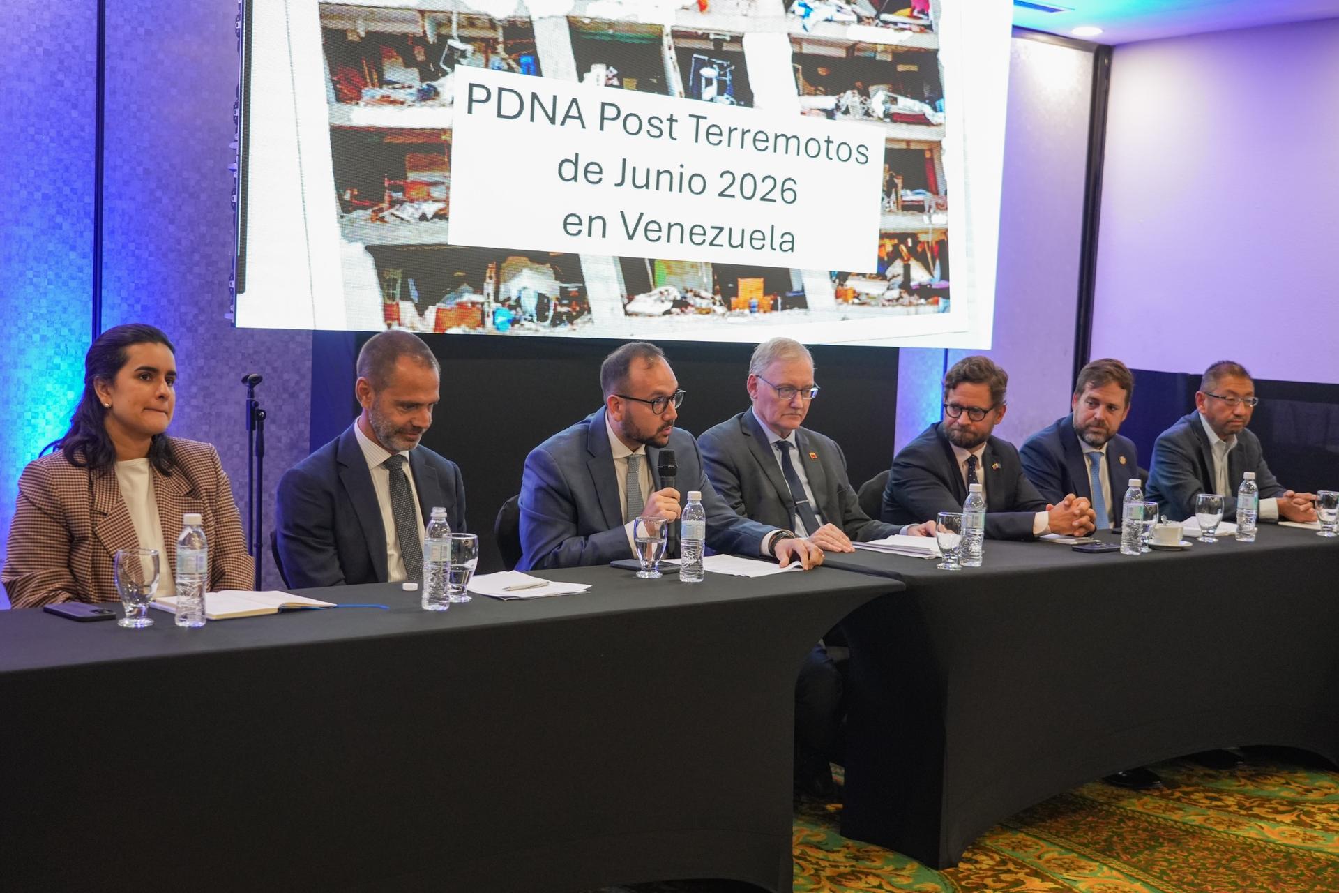 Panel of speakers seated at a long table on stage; projection screen behind shows a PDNA banner.