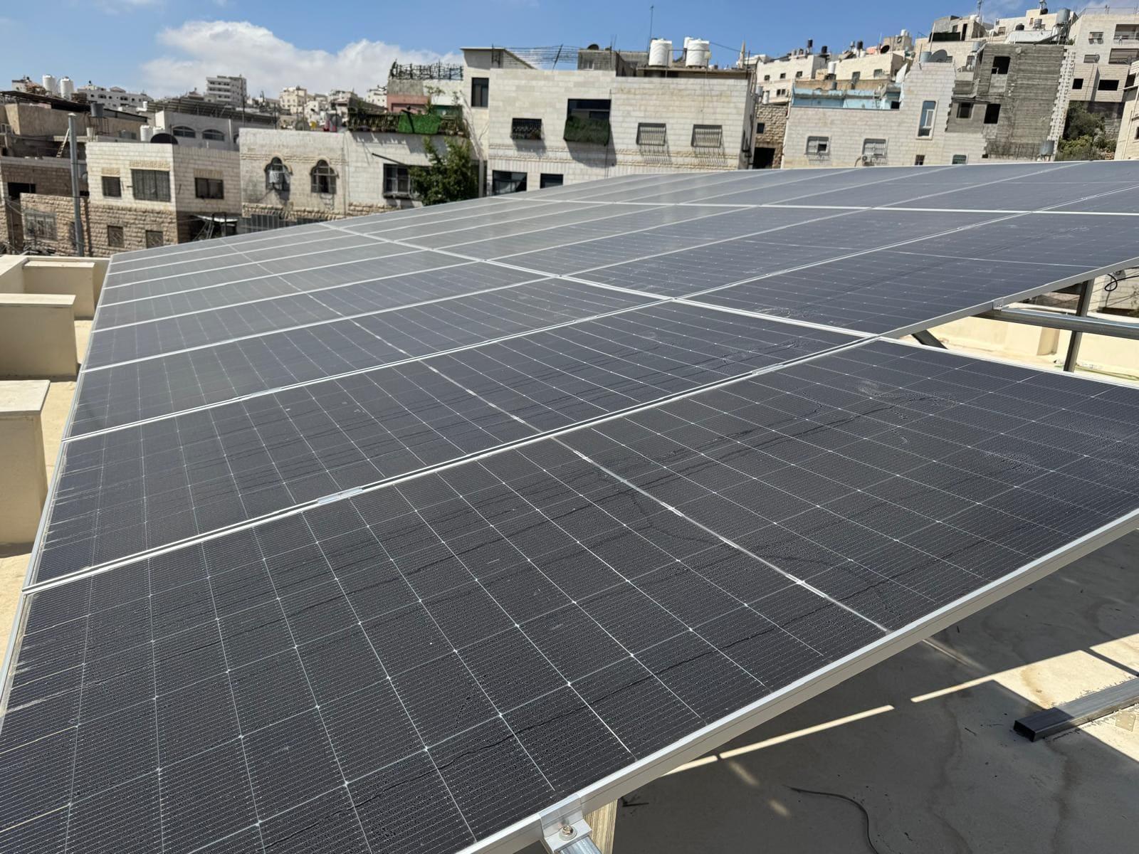 Row of solar panels on a flat rooftop with city buildings in the background.