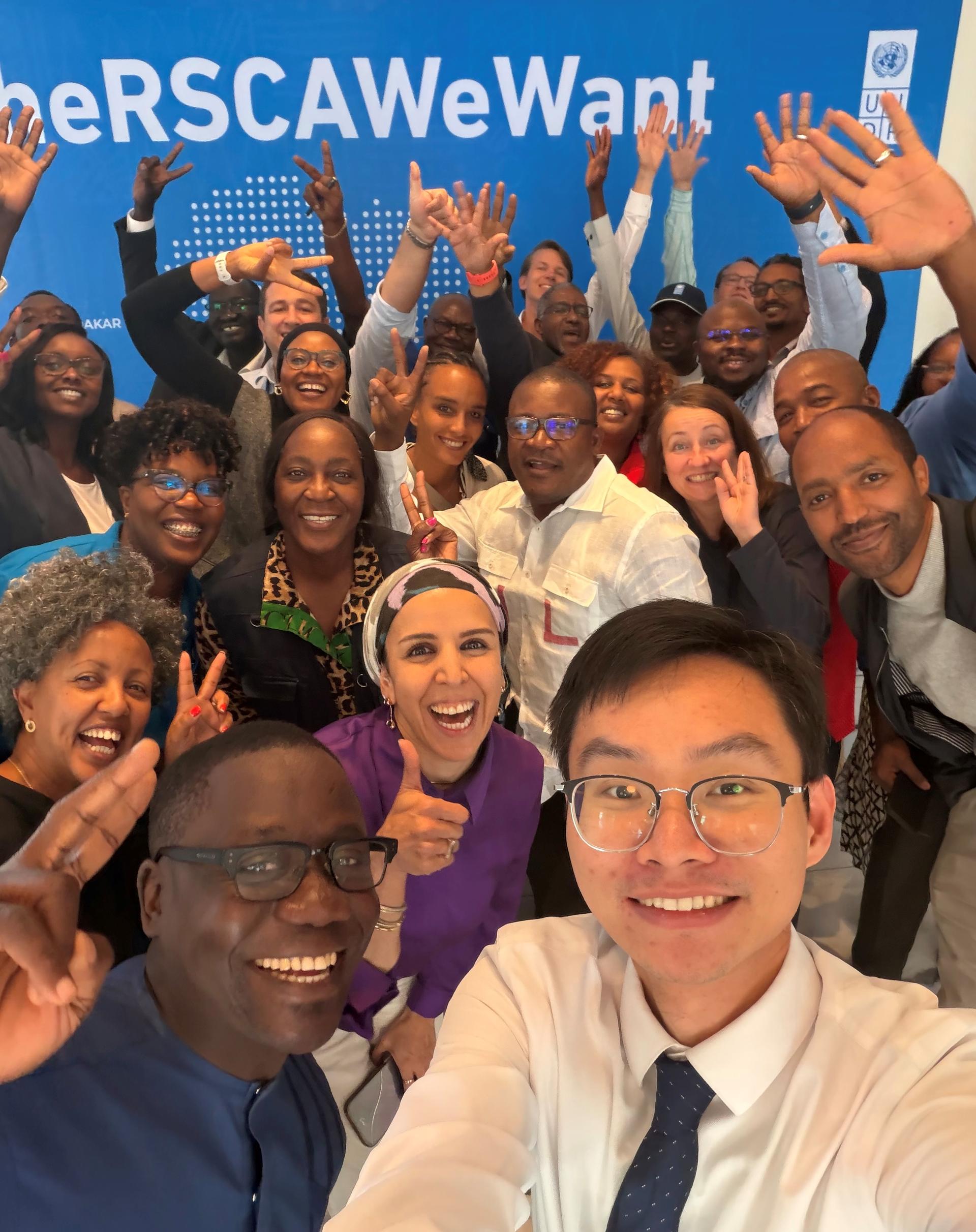 Group photo of diverse, smiling people raising hands in front of a blue banner.