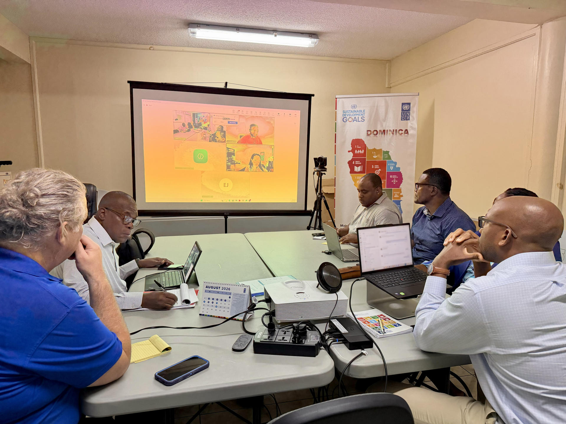 Photo: Group of colleagues around a conference table with virtual participants on the screen.