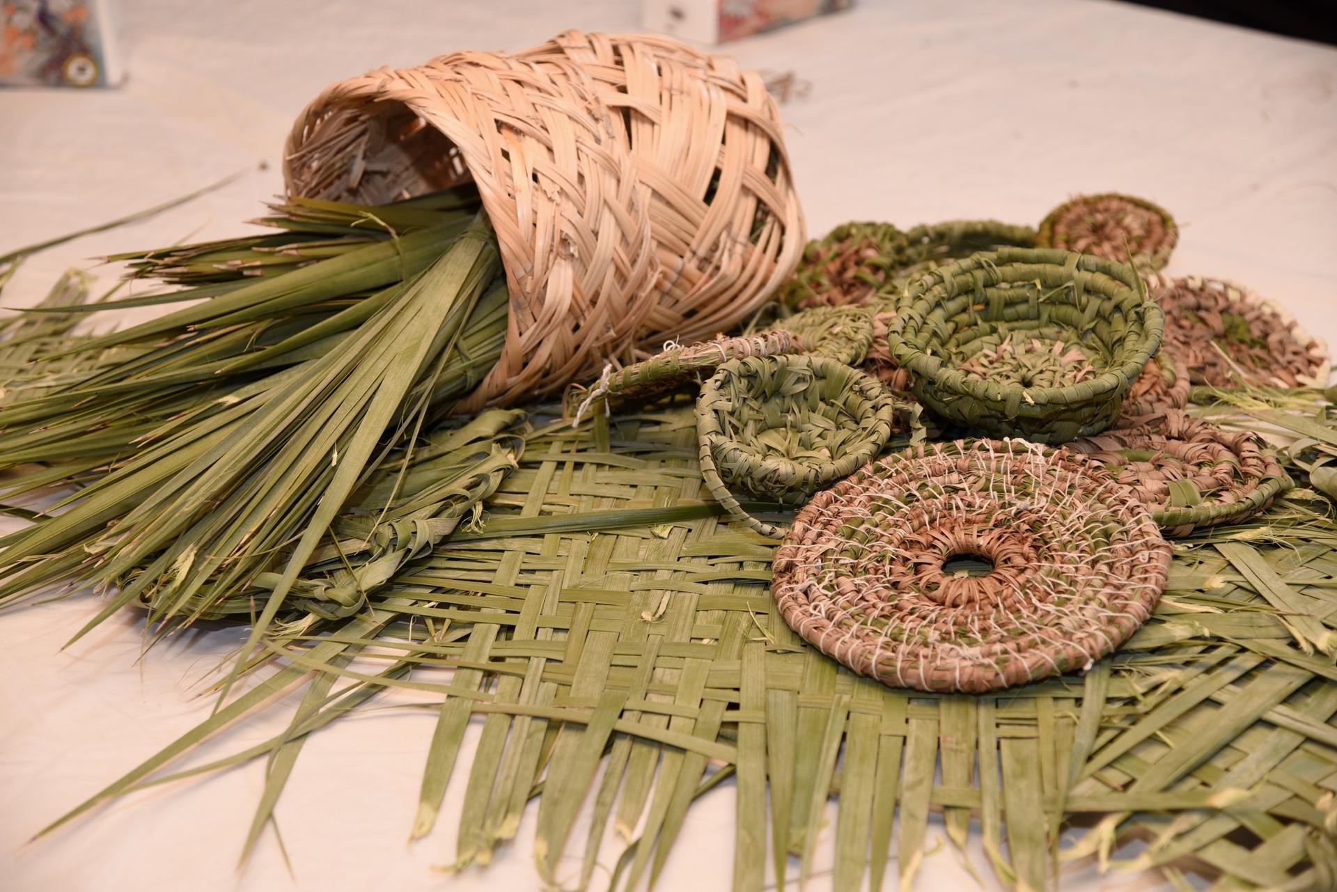 Green ring-shaped crackers with sesame seeds on a woven mat beside a small leafy bouquet tied with twine.