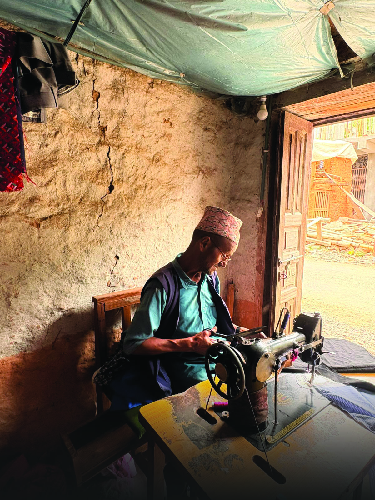 Person in turquoise shirt sits at a sewing machine in a rustic room under a green tarp.