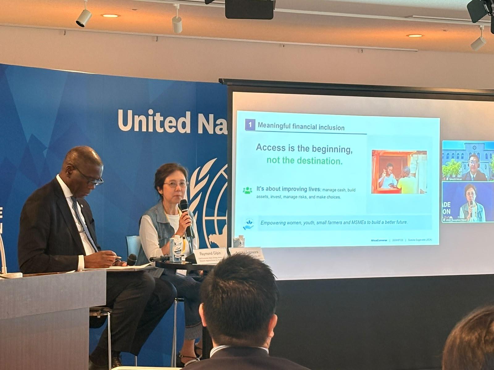 Photograph of a United Nations conference panel with speakers at a podium and a slide on screen.