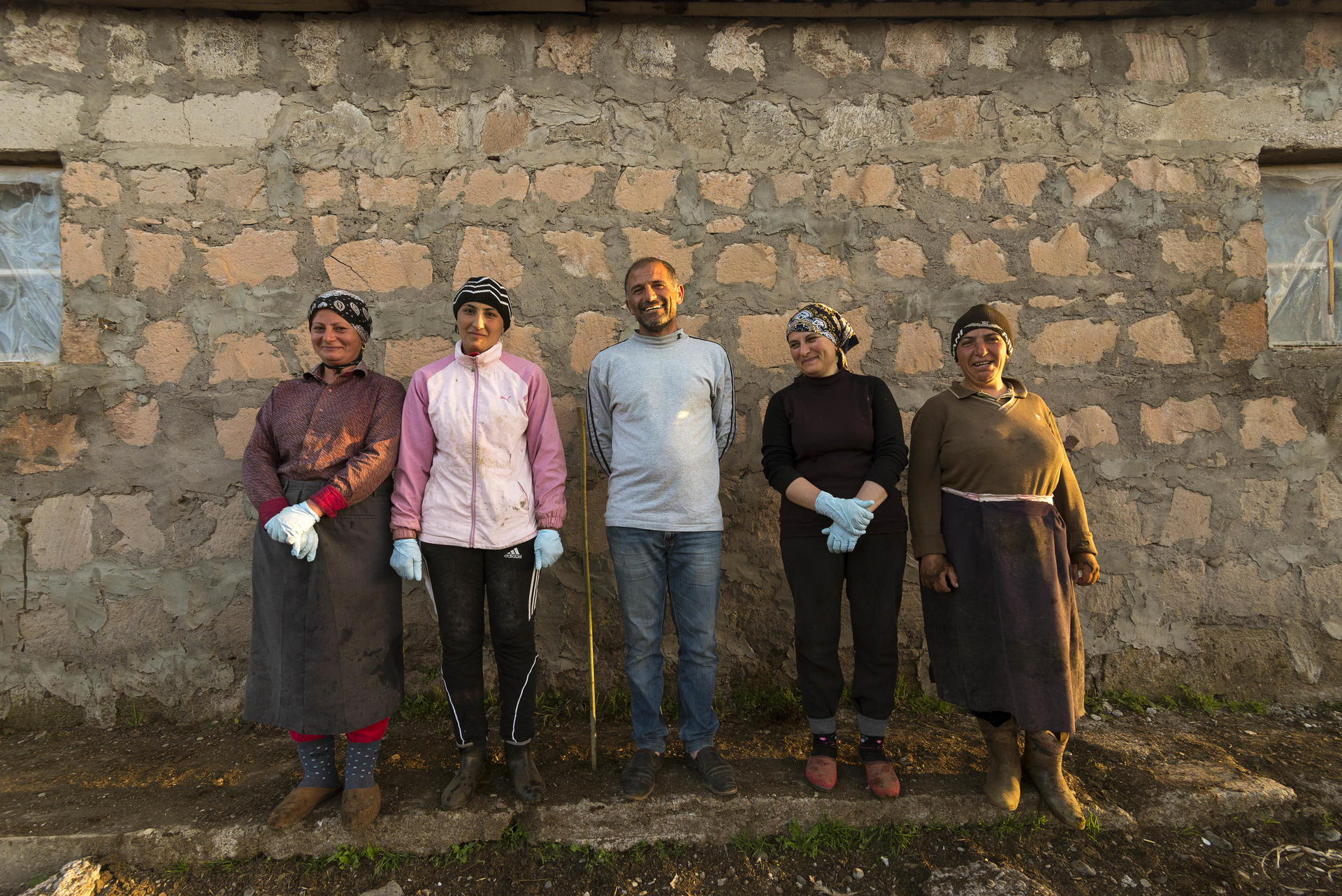 Five adults standing in a line in front of a rustic stone wall outdoors.