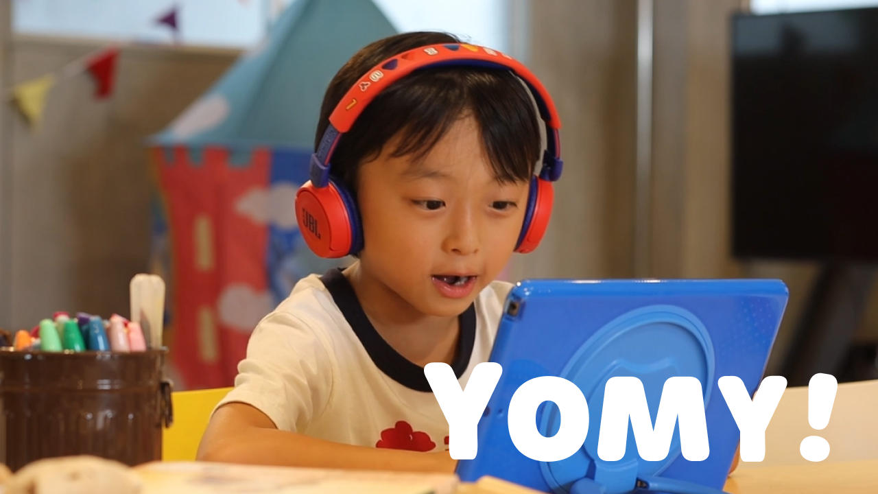 Photo of a young child wearing red headphones, drawing at a colorful classroom table.