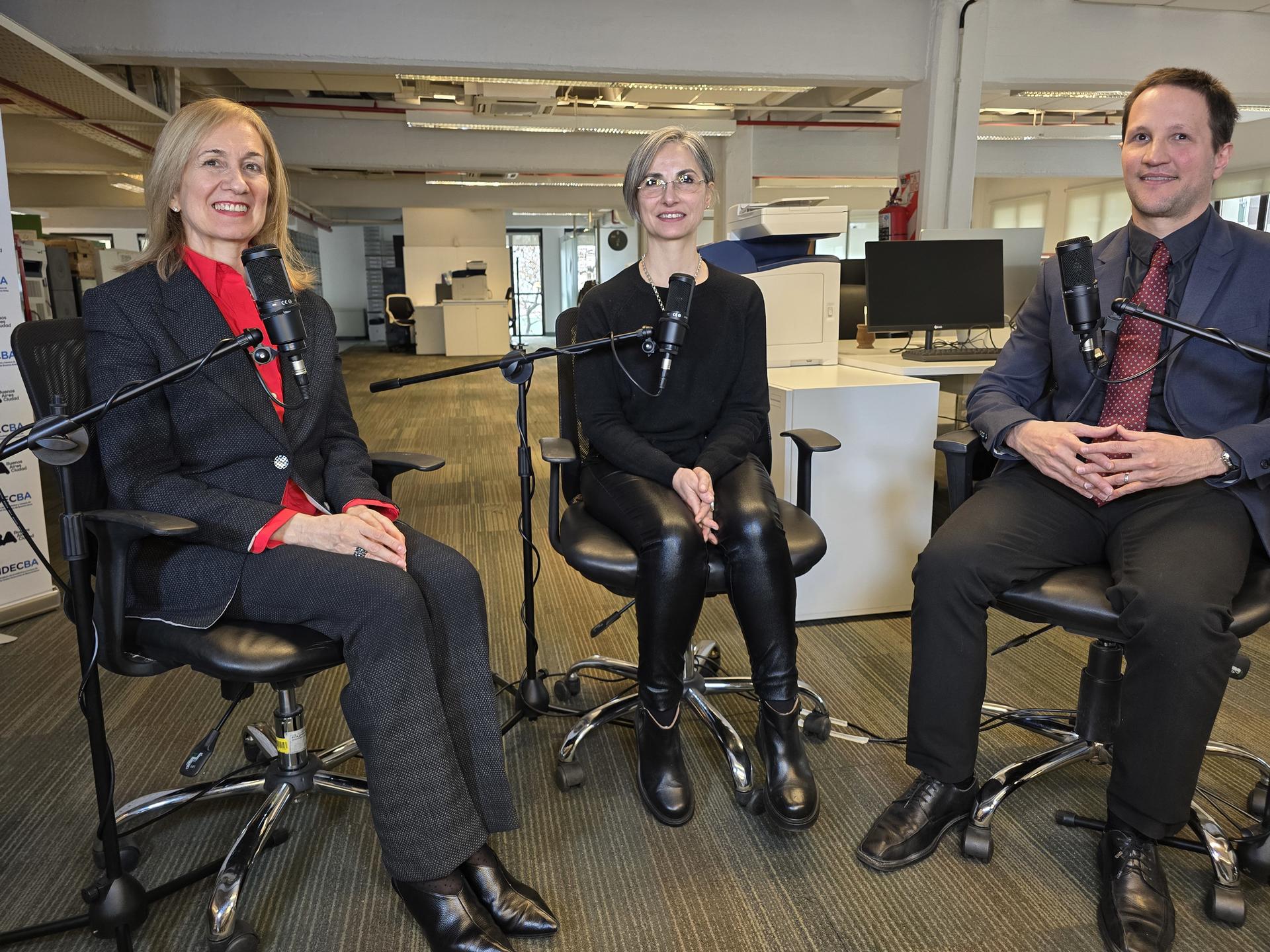 Three professionals (two women, one man) seated in office chairs, smiling.