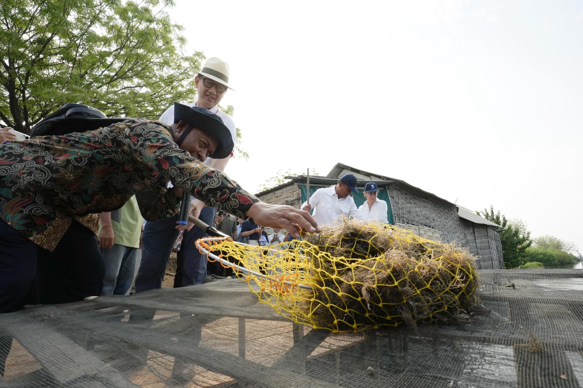 A group of people in hats lean over a large yellow woven straw sculpture outdoors.