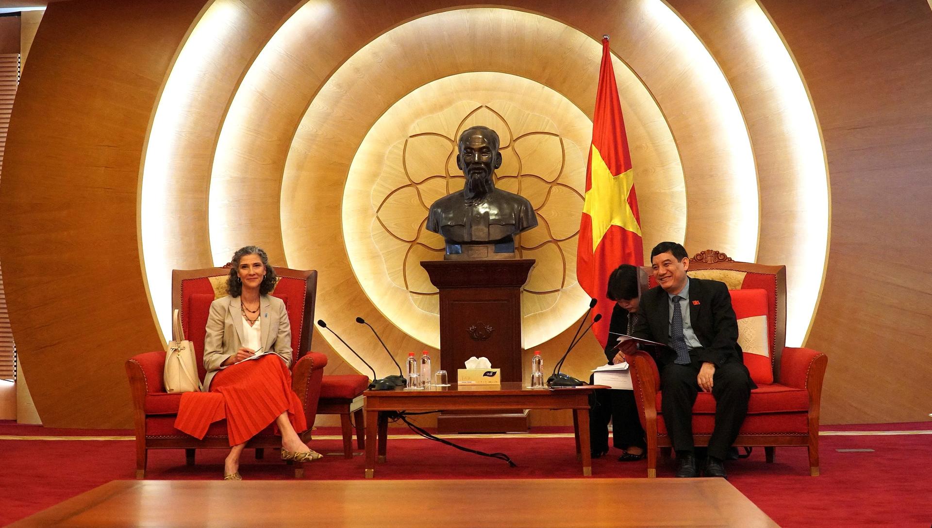 Three people sit on red chairs on stage; podium with Buddha statue and circular light rings behind.