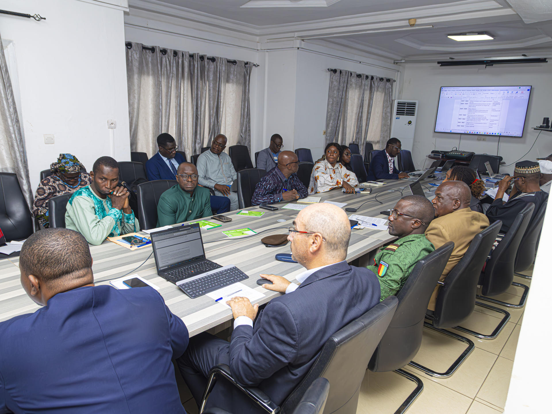 Professionals seated around a long conference table in a meeting room; presentation on screen.