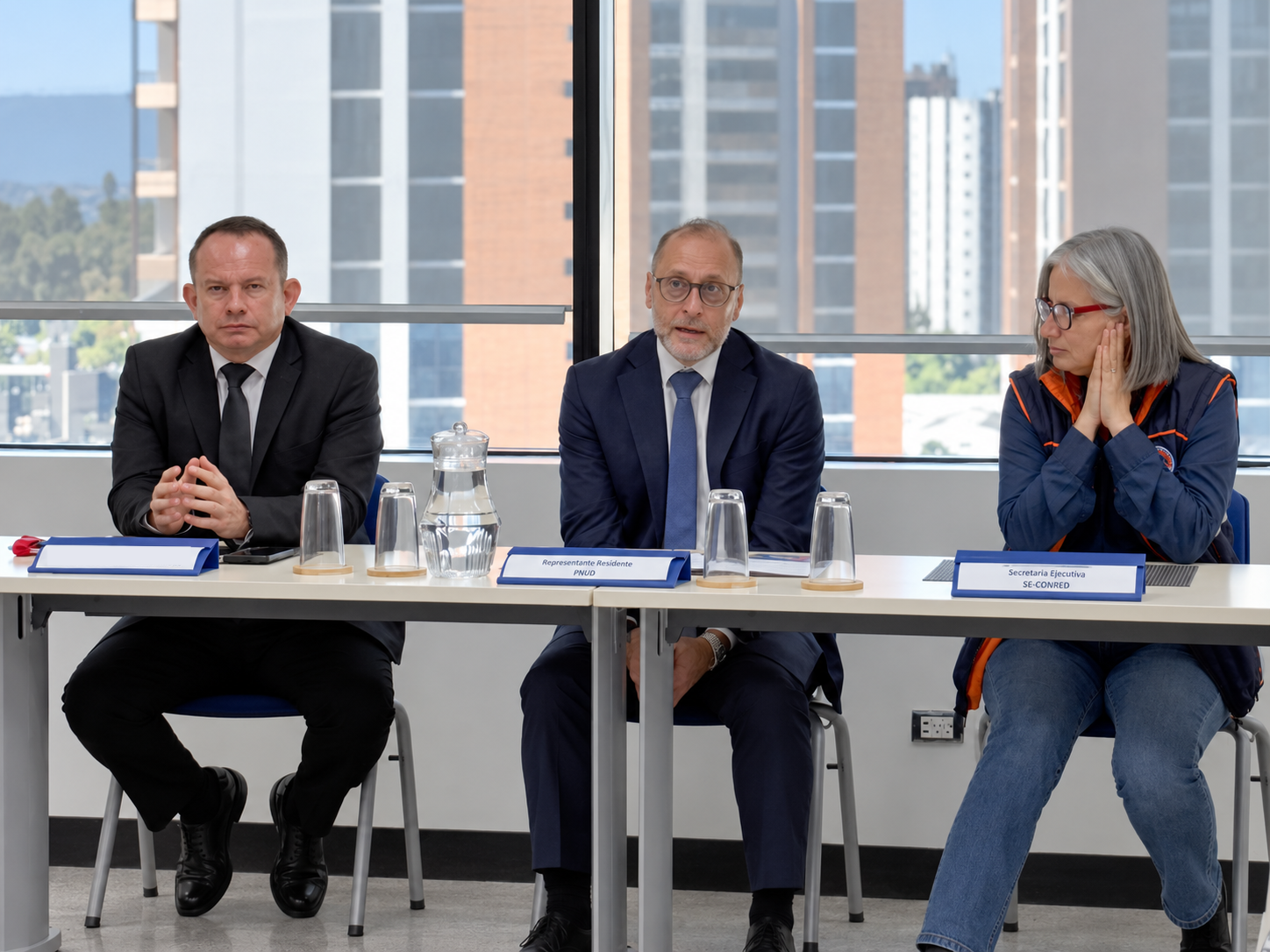 Photograph: three panelists seated at a conference table with microphones.