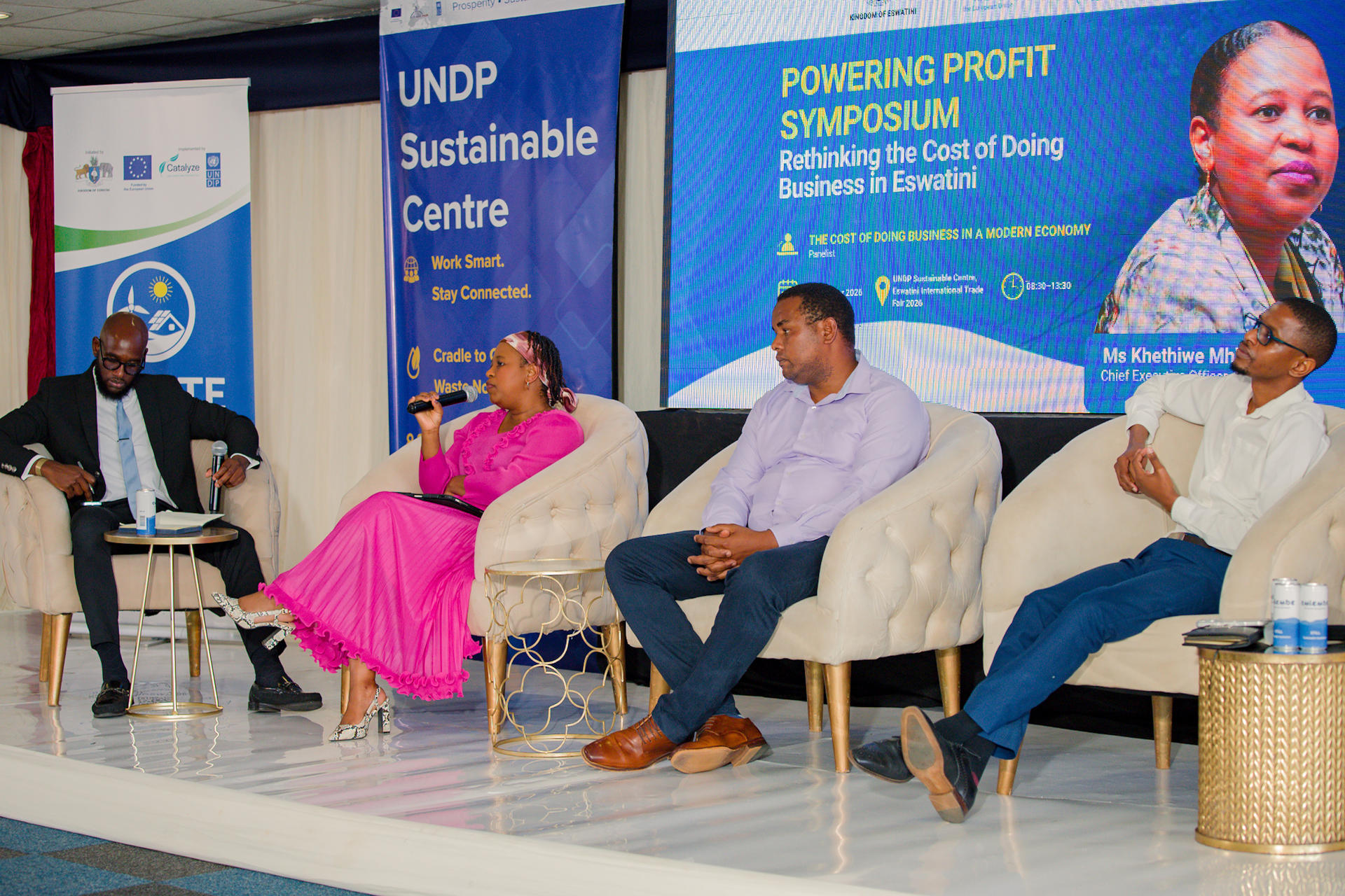 Four panelists seated on stage beside a pool, with UNDP banners in the background.
