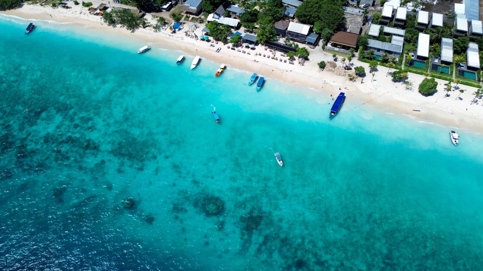 Aerial view of tropical beach with turquoise water, white sand, palm-lined shore, and boats.