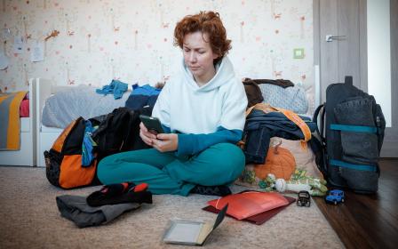A woman uses a mobile phone seated on the floor surrounded by personal belongings