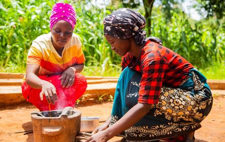 Women in traditional dress crouch over cookstove