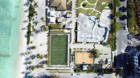 aerial image of hulhumale city showing a tennis court, skating rink, restaurant rooftop and roads with vehicles adjacent to buildings and the sea on the opposite end