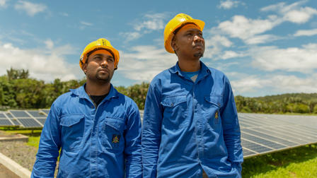 Men in hard hats and overalls stand next to solar panels