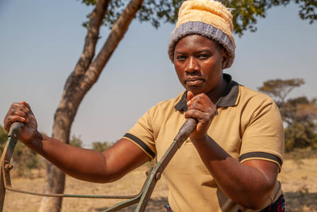 A woman holding a ripper in a farm field used for farming.