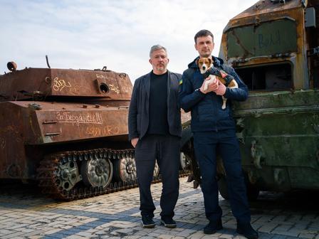 two men and a dog standing in front of a truck