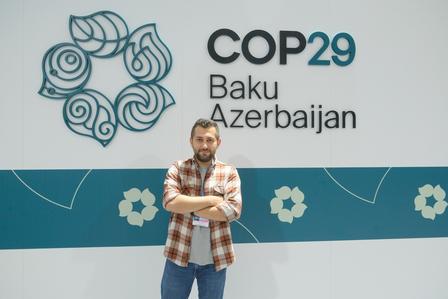 Young man standing in front of a COP29 sign