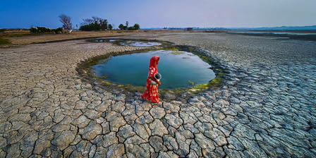 a woman walking on a cracked soil to find safe drinking water