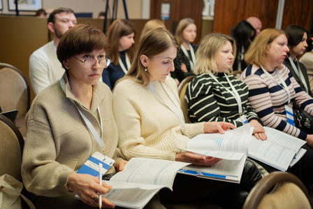 Women attendees at a conference session, focused and engaged, reviewing printed materials and taking notes.