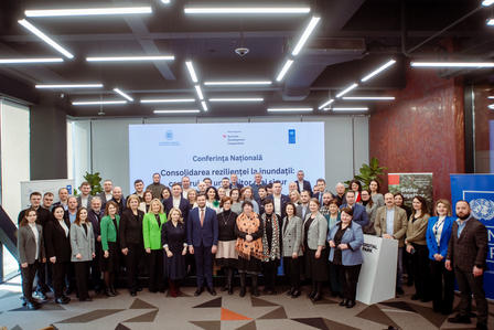 A large group of people stands together in a conference-like setting, smiling.