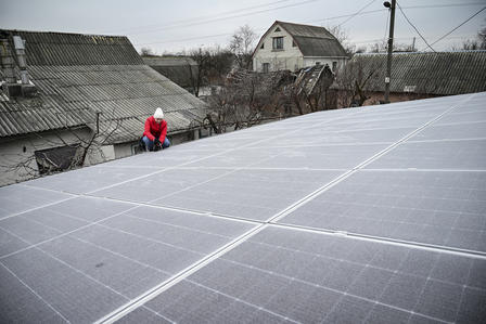 A worker adjusts solar panels on a rooftop with houses in the background.