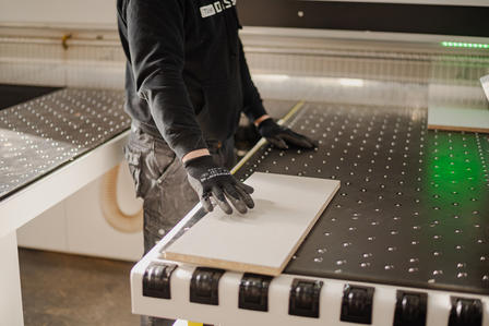 A person wearing gloves operates a machine, positioning a sheet on a work table.