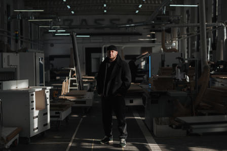 A person in dark clothing stands in a dimly lit workshop surrounded by machinery.
