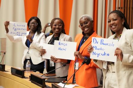 Four women hold signs in a conference room, smiling and posing together.