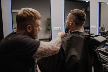 A barber prepares to cut the hair of a client, who is seated with a black cape.
