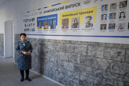 A woman in a blue outfit stands beside an informational wall display in a hallway.