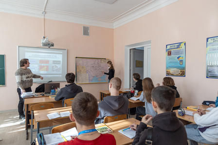 A classroom scene with students attentively listening to a presentation, with a map displayed.