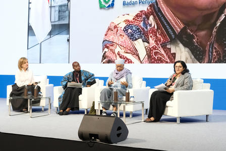 Four women sit on white chairs during a panel discussion on a stage.