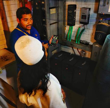 A technician explaining electrical equipment to another person in a utility room.
