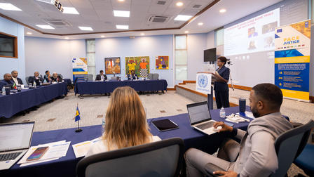 A conference room with attendees seated at a large table; a speaker presenting.