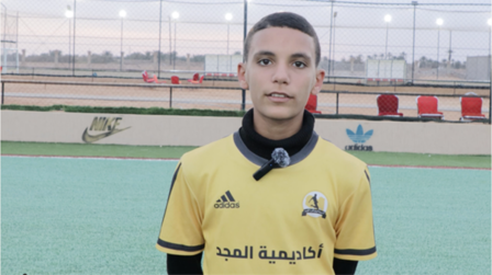 A young boy wearing a yellow sports jersey stands on a soccer field.