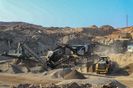 Construction site with machinery processing gravel and sand under a clear blue sky.