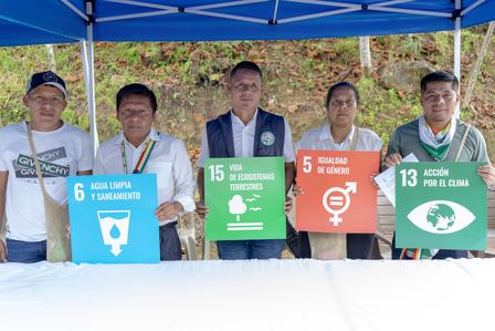 Five individuals hold signs representing various sustainable development goals under a blue tent.